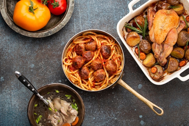 Dining table with traditional tasty homemade dishes: chicken soup, meatballs with spaghetti, roasted chicken with potatoes. Classic home natural comfort food for family meal dinner, top view