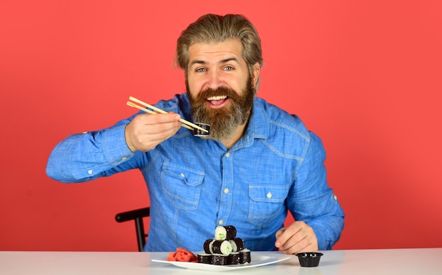 Foto cena a casa hipster mangia sushi con le bacchette gustoso rotolo di sushi cibo tradizionale e sano in giappone piatto di sushi giapponese uomo che mangia cibo tradizionale giapponese con le bacchette