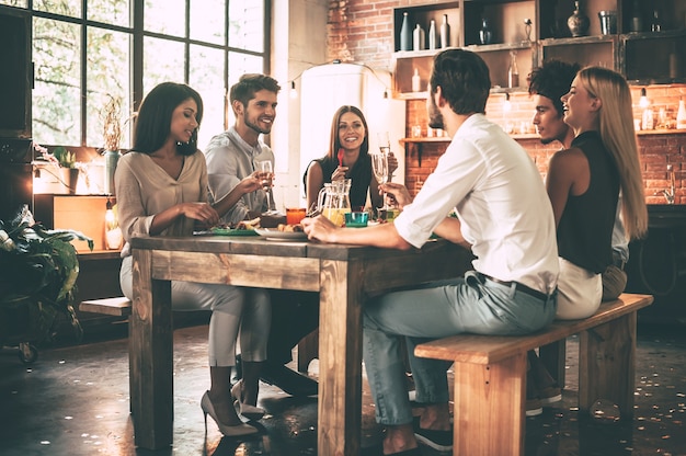 Dinner party. Group of cheerful young people enjoying dinner while sitting on the kitchen together