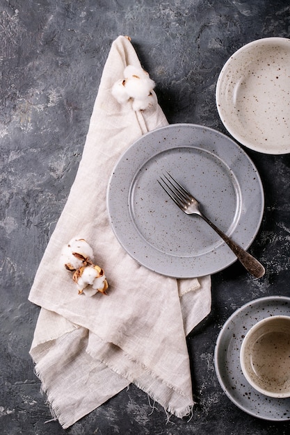 Photo dinner place setting. a blue modern ceramic plate with silver fork decorated with cotton flower over dark texture surface. top view, flat lay.