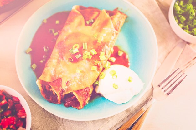 Dinner plate with Chicken enchiladas garnished with green onions and sour cream.