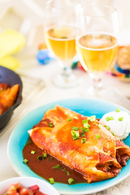 Dinner plate with Chicken enchiladas garnished with green onions and sour cream.