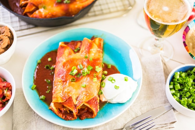 Dinner plate with Chicken enchiladas garnished with green onions and sour cream.