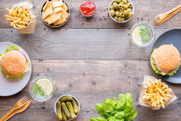 Dinner table with burger, french fries, vegetables, sauces, snacks and lemonade