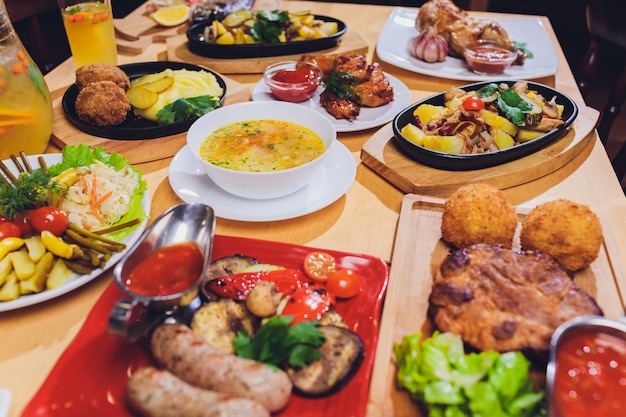 Dinner table with meat grill, roast new potatoes, vegetables, salads, sauces, snacks and lemonade, top view.