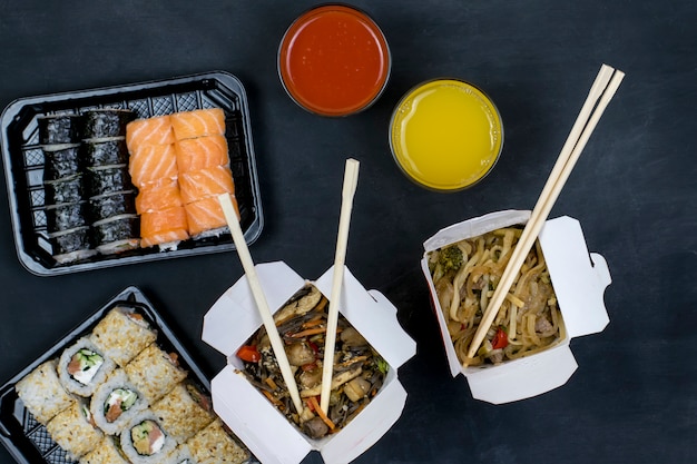 Dinner for two. Delivery of Japanese food. Sushi and hot noodles with vegetables on a black background