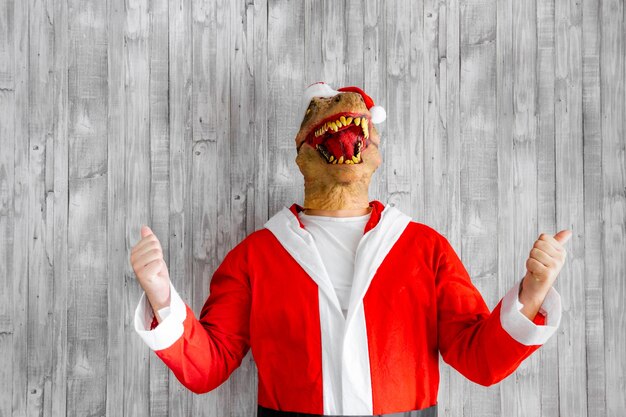 Динозавр, одетый как Санта-Клаус, с поднятыми руками, делает победный жест.