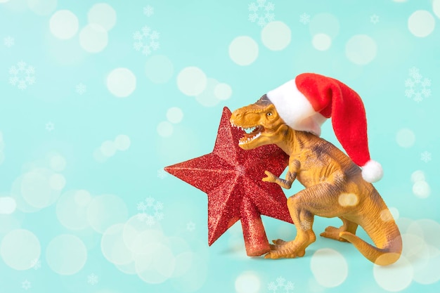 Dinosaur Rex in red Santa Claus hat holds star in its paws on blue background New Years Eve or Christmas Eve Art holiday card Creative idea for Merry xmas concept.