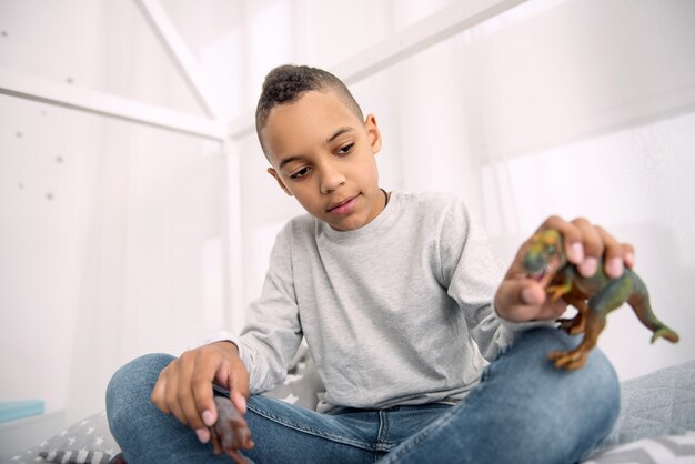 Dinosaur toy. Pretty afro american boy looking down while holding dinosaurs toys