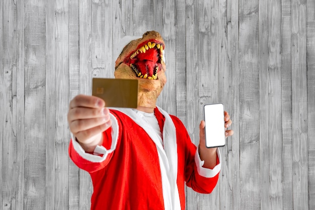 Dinosaurus vermomd als kerstman met creditcard en mobiele telefoon in de hand