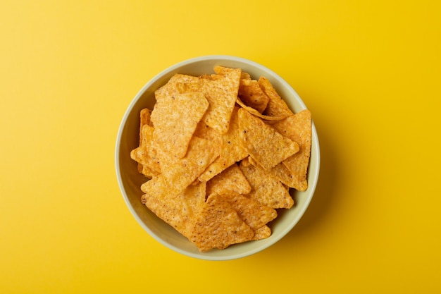 Direct boven close-up shot van nachochips in kom op gele achtergrond met kopieerruimte. ongewijzigde, ongezonde voeding, snack en knapperige snack.