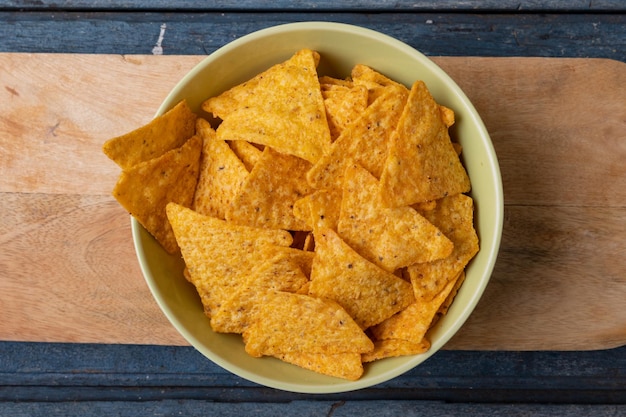 Direct boven close-up shot van nachochips in kom op serveerplank aan houten tafel. ongewijzigde, ongezonde voeding, snack en knapperige snack.