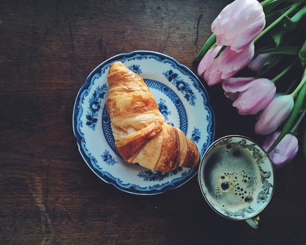 Direct boven croissant en koffie met roze tulpen op tafel.