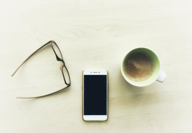 Direct boven een foto van een smartphone met koffie en een bril op tafel