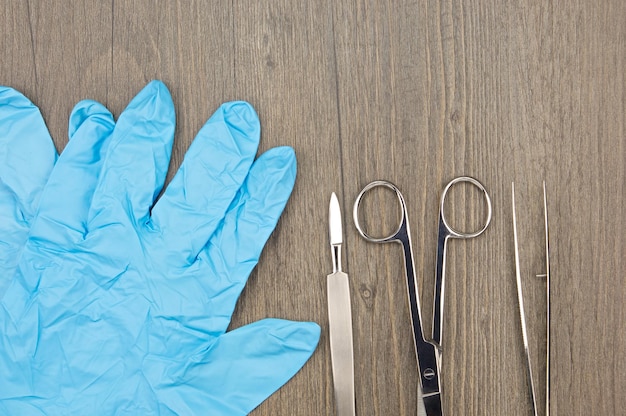 Direct boven opname van blauwe chirurgische handschoenen met chirurgische apparatuur op een houten tafel