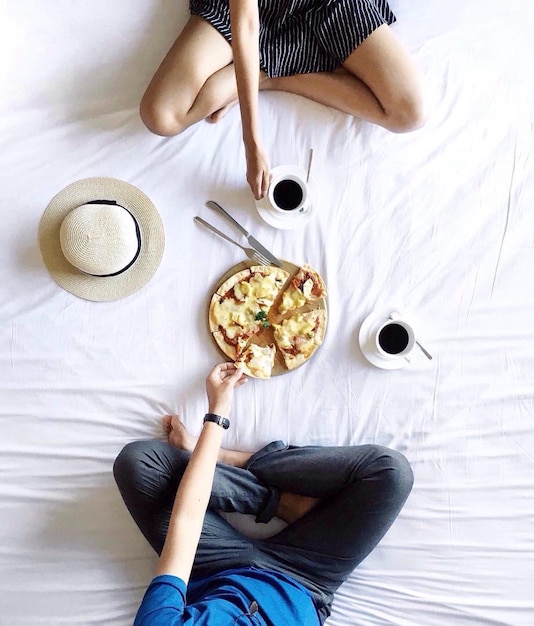 Direct boven opname van man en vrouw met pizza en koffiekopjes op bed