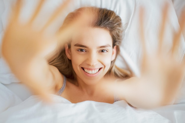Direct boven portret van vrolijke vrouw die in bed gebaren maakt