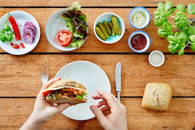 Direct boven schot van geknipte handen die een hamburger op tafel houden