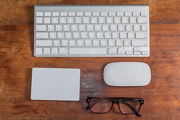 Foto direct boven schot van het toetsenbord van de computer met muis en bril op een houten tafel