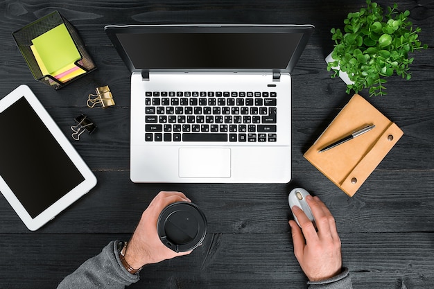 Direct boven weergave van menselijke handen die op laptop typen. Laptop, digitale tablet, agenda, koffiekopje en potplant op bureau. Man aan het werk vanuit huis.