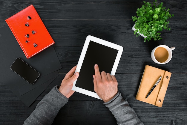 Direct boven weergave van menselijke handen met digitale tablet. digitale tablet, agenda, koffiekopje en potplant op bureau. man aan het werk vanuit huis.