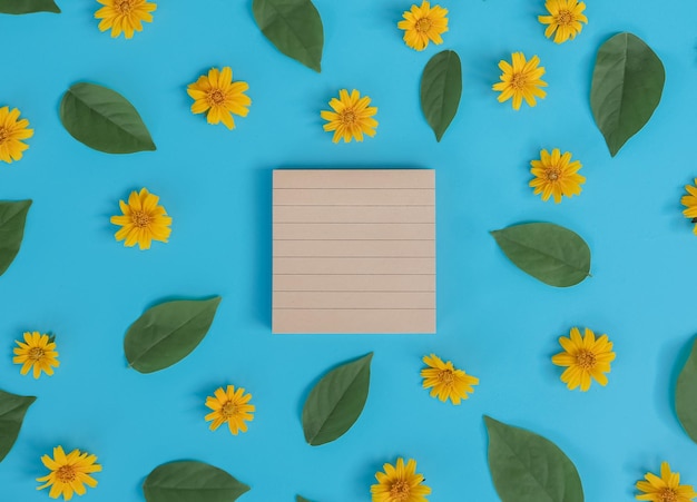 Direct boven zicht van een leeg notitieboek met oranje bloem en groen blad op blauwe achtergrond