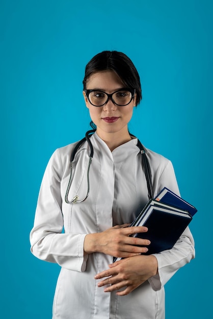 Прямой взгляд на девушку-врача-стажера с книгами в руках в платье на изолированном простом студийном фоне