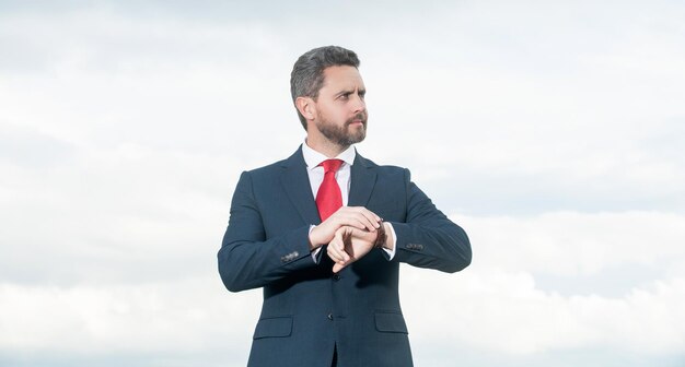 Directeur in zakelijk pak die de tijd controleert op de hemelachtergrond