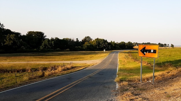 Photo directional sign by empty country road against sky