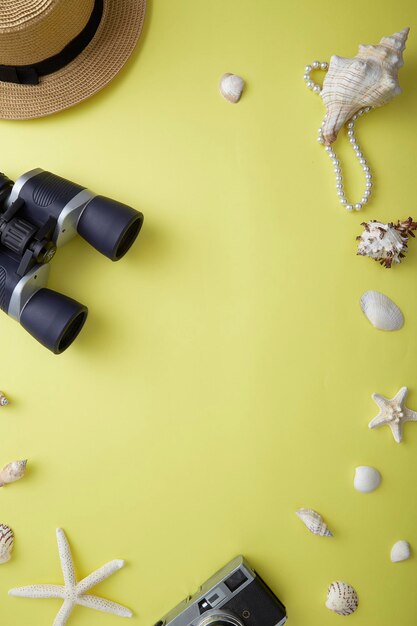 Photo directly above of hat by binoculars and seashells over yellow background