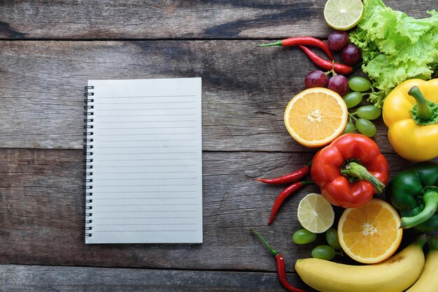 Photo directly above shot of blank book by fruits and vegetables on wooden table