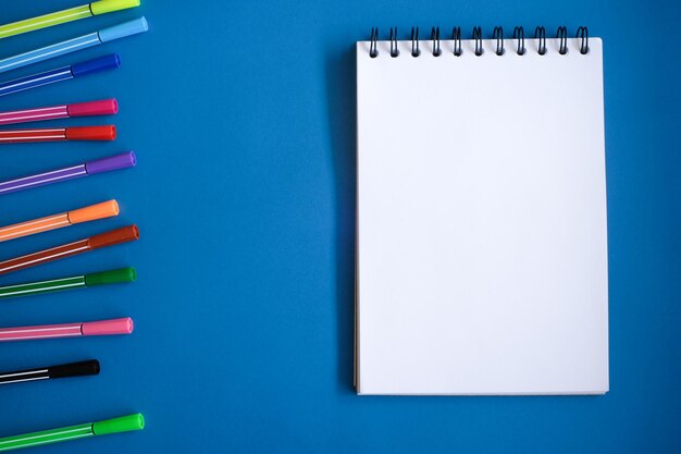 Directly above shot of blank note pad with colored pencils on blue table