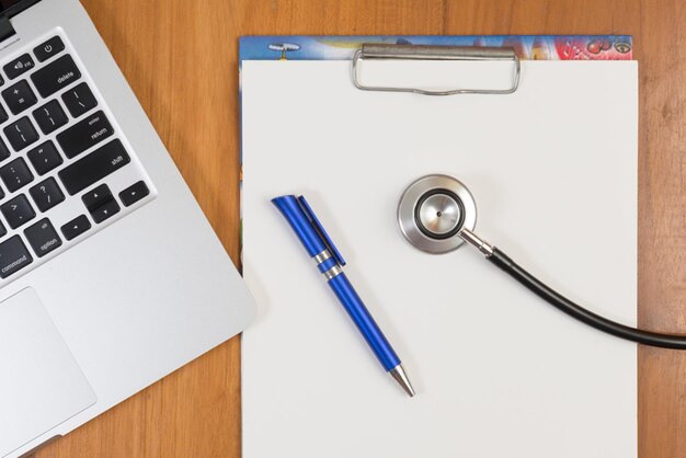 Photo directly above shot of blank paper with laptop and stethoscope on table