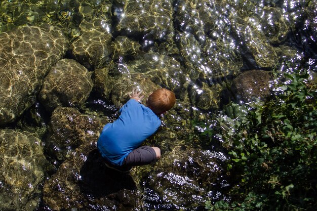 Photo directly above shot of boy crouching on rocks in river