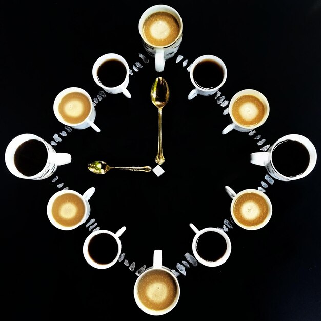 Foto direttamente sopra la foto di tazze di caffè disposte in forma di orologio contro uno sfondo nero