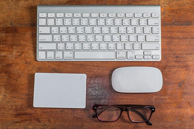 Foto scatto direttamente sopra della tastiera del computer con mouse e occhiali su un tavolo di legno