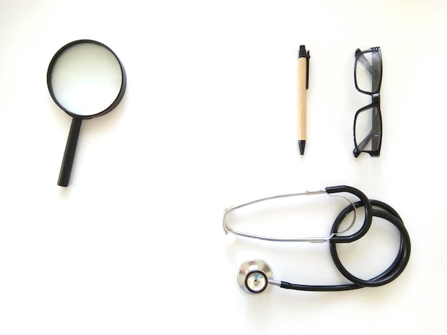 Directly above shot of eyeglasses and pen with stethoscope by magnifying glass over white background