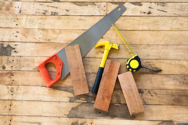 Photo directly above shot of hammer with hand saw and tape measure on wooden plank