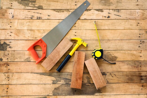 Photo directly above shot of hammer with hand saw and tape measure on wooden plank