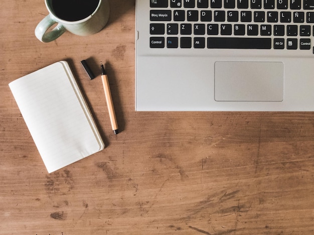 directly above shot of laptop by coffee cup and notepad on table