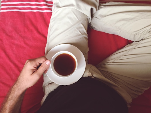 Directly above shot of man holding tea cup on bed