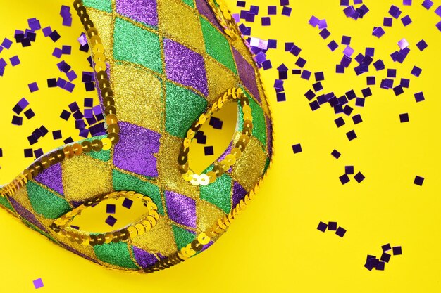 Directly above shot of mask with confetti over yellow background