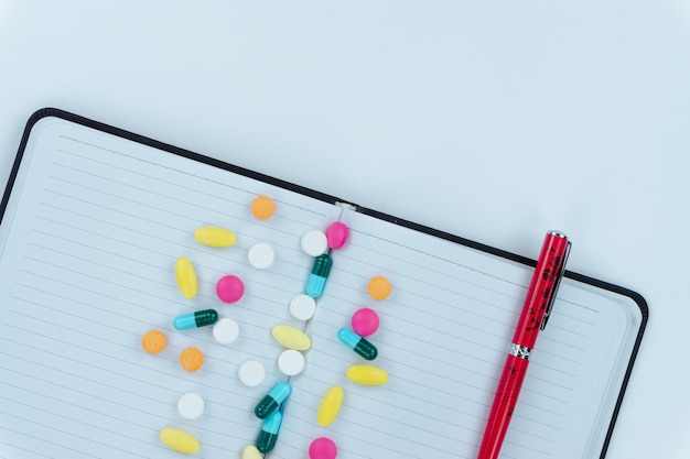 Directly above shot of multi colored pills by spiral notebook on table