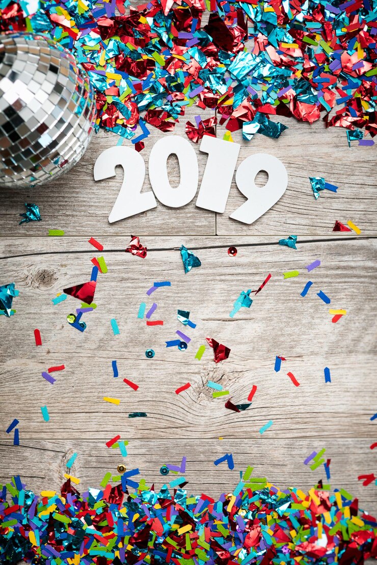 फोटो directly above shot of number 2019 and confetti by disco ball on wooden table