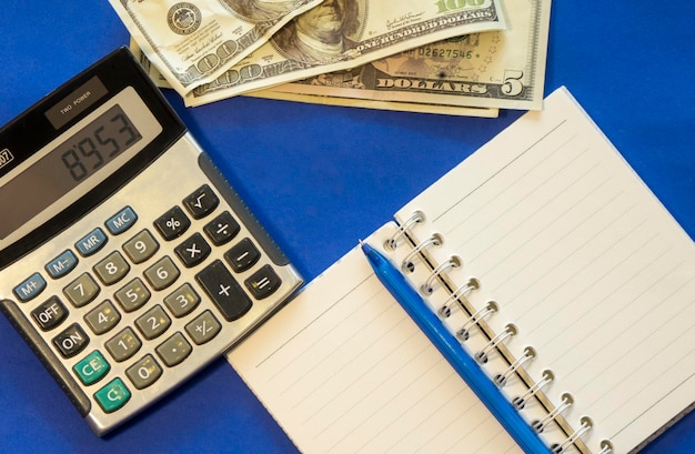 Directly above shot of paper currency with diary and calculator on blue background