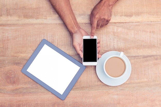 Directly above shot of person using smart phone by coffee and tablet on table