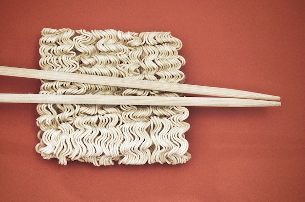 Photo directly above shot of raw noodles with chopsticks on brown background