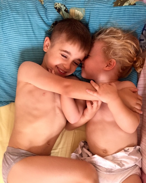 Photo directly above shot of shirtless siblings lying on bed