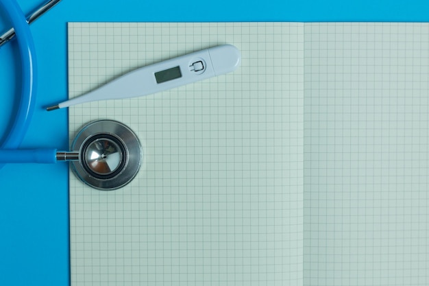 Directly above shot of stethoscope and thermometer by paper against blue background
