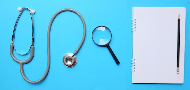 Directly above shot of stethoscope with book and magnifying glass over blue background